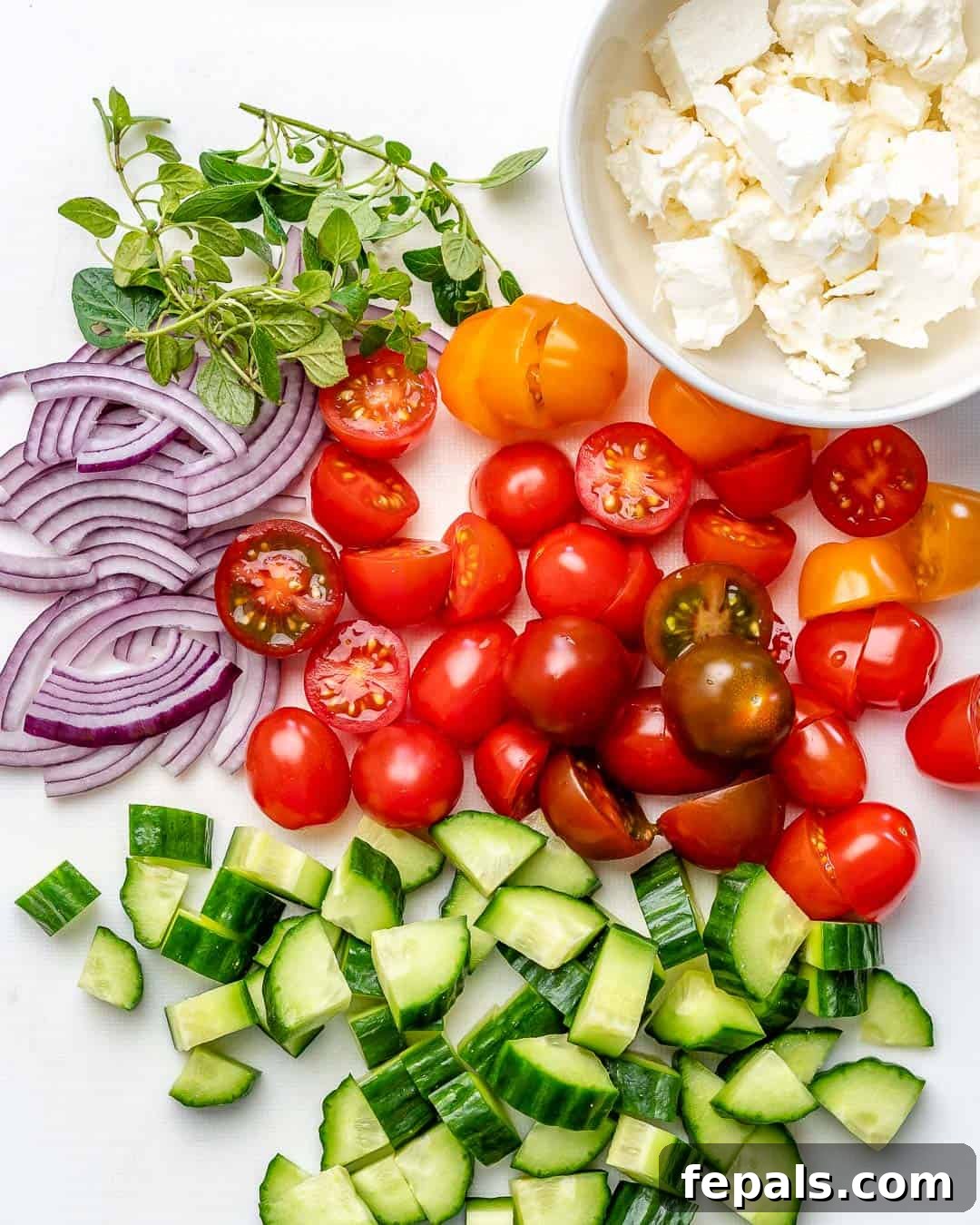 Zesty Mediterranean Chicken Salad 4 Assorted fresh vegetables for Greek salad, including vibrant cherry tomatoes, crisp cucumbers, thinly sliced red onion, and briny Kalamata olives, alongside crumbled feta cheese, all neatly arranged on a cutting board, ready for preparation.