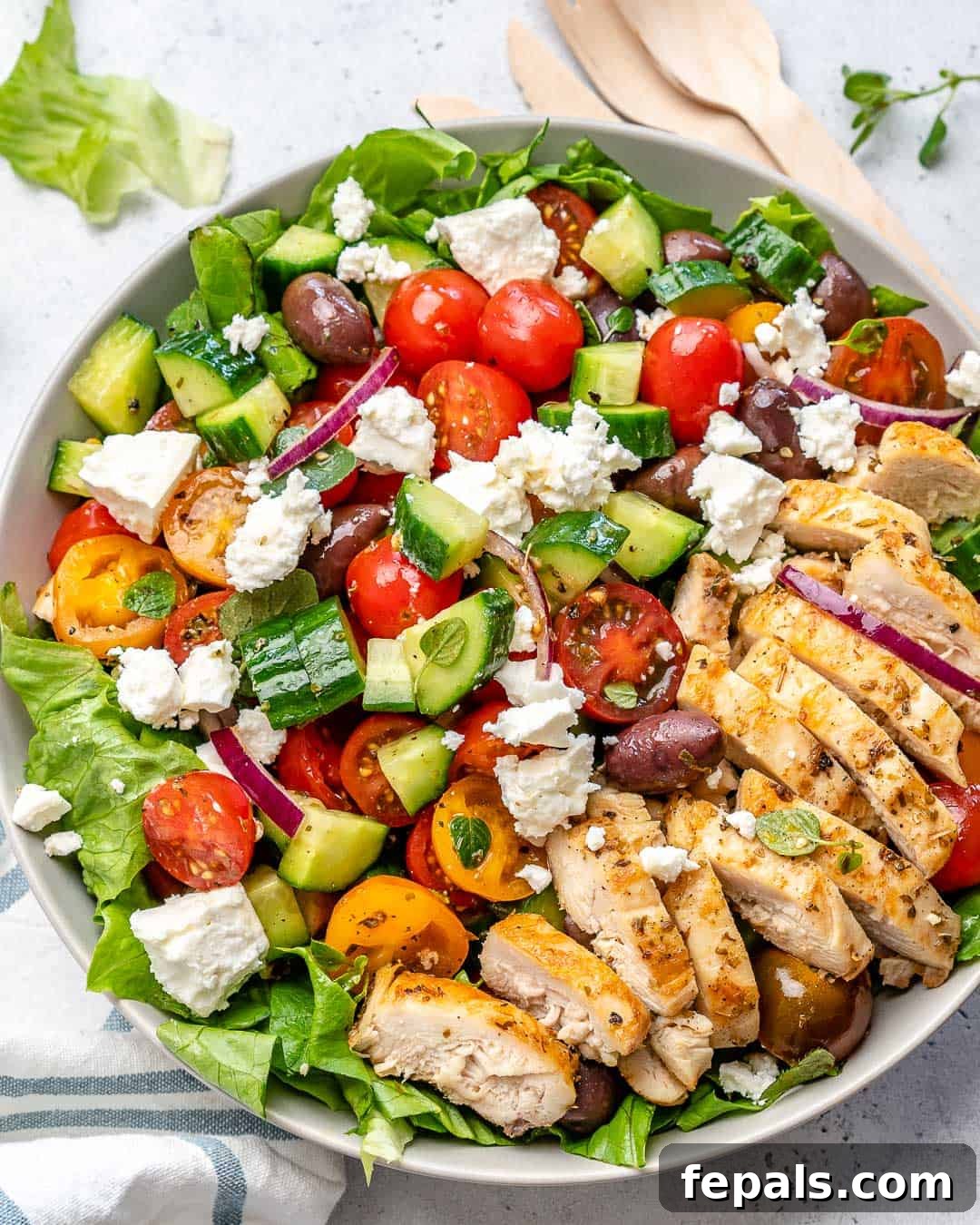 Zesty Mediterranean Chicken Salad 6 Top view of a beautifully prepared Greek salad with succulent chicken slices and crumbled feta cheese, elegantly garnished with fresh herbs, presented in a pristine white bowl.
