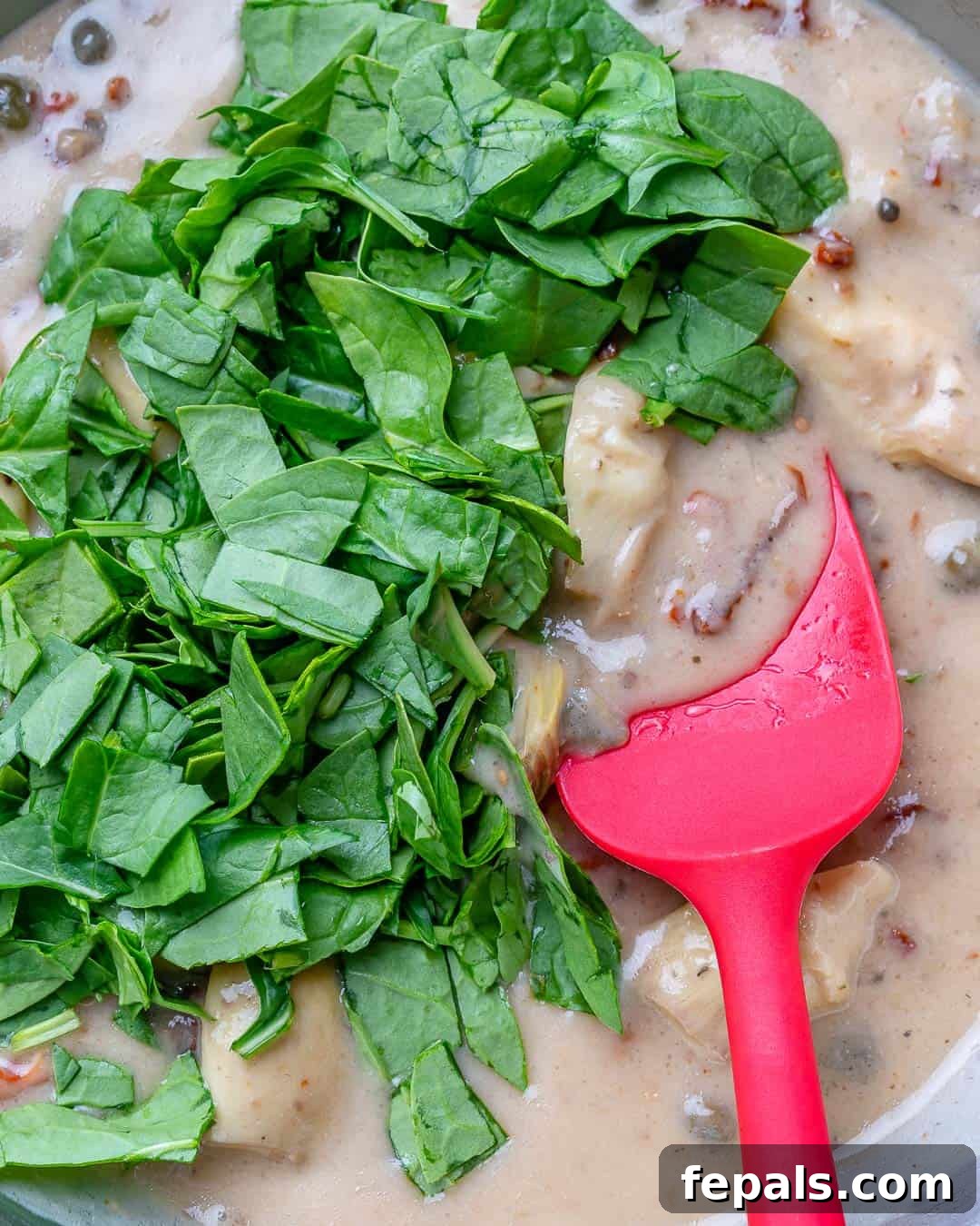 Creamy Tuscan Chicken Delight 4 Fresh spinach being stirred into a rich, creamy Tuscan sauce in a skillet, combining with sun-dried tomatoes, artichokes, and capers.