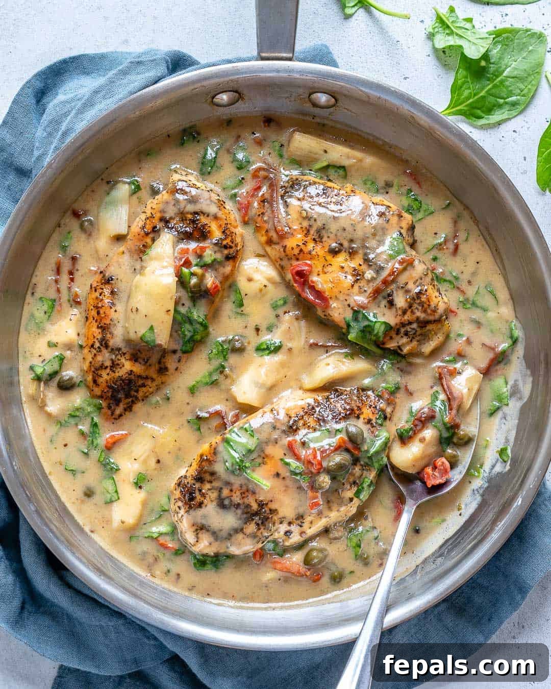Creamy Tuscan Chicken Delight 7 Top view of a skillet showcasing three pieces of creamy Tuscan chicken, perfectly sauced and ready to be served, with a spoon resting in the rich sauce.