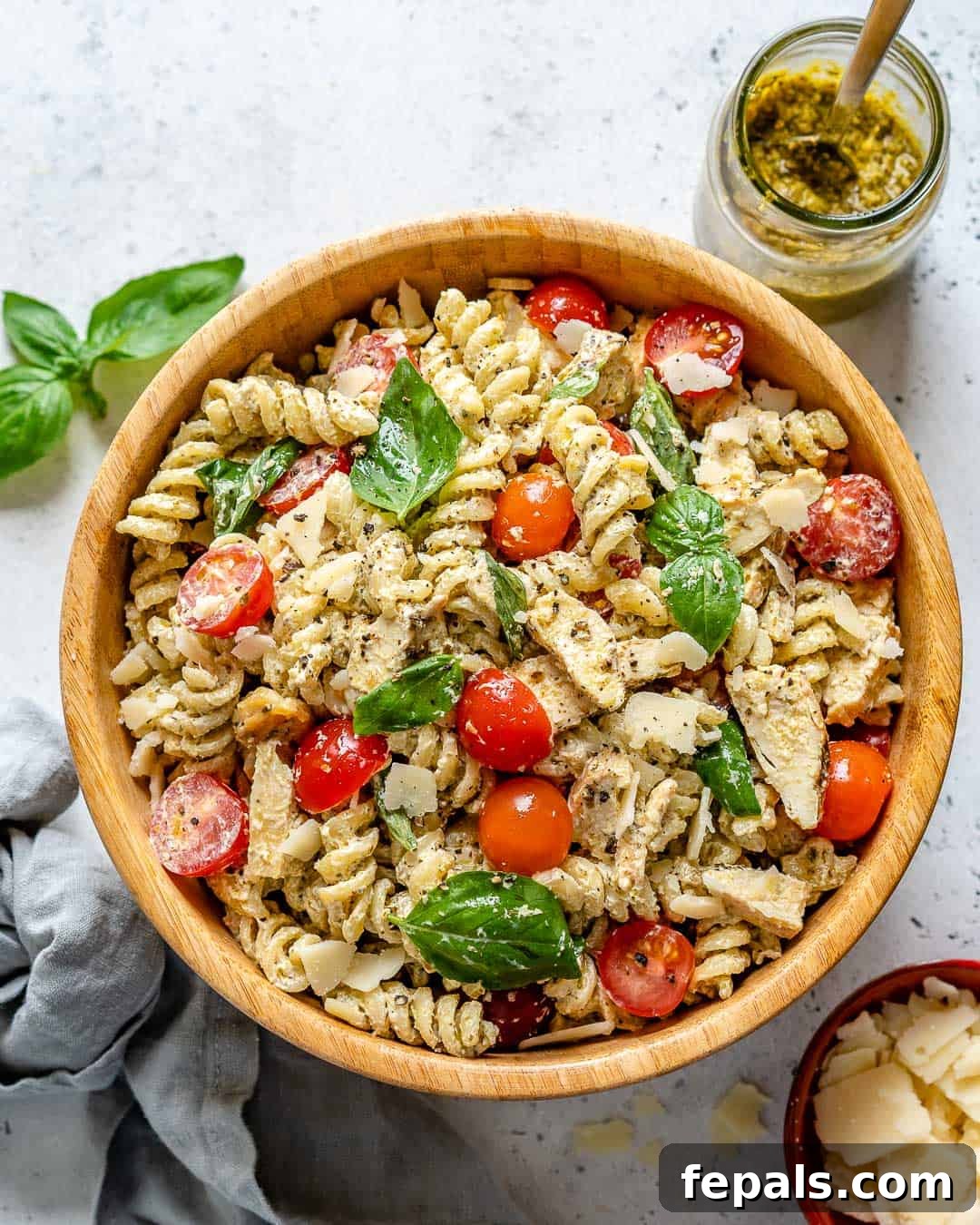 A beautifully presented bowl of creamy chicken pesto pasta salad, garnished with fresh basil leaves and a sprinkle of Parmesan cheese.
