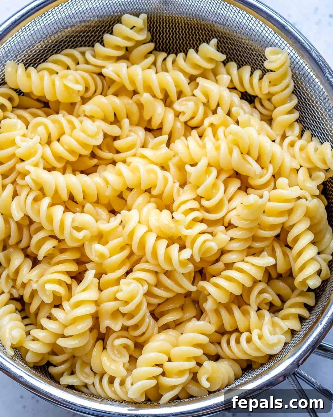 Freshly cooked al dente pasta draining in a colander under cold water, ready for the pasta salad assembly.
