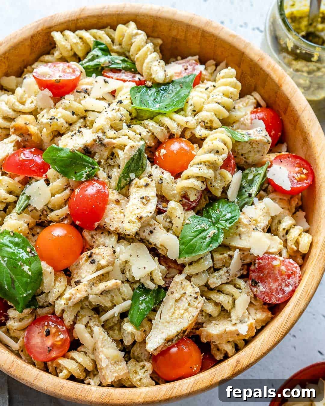 A vibrant bowl of creamy chicken pesto pasta salad, richly coated in dressing and adorned with fresh cherry tomatoes and basil.