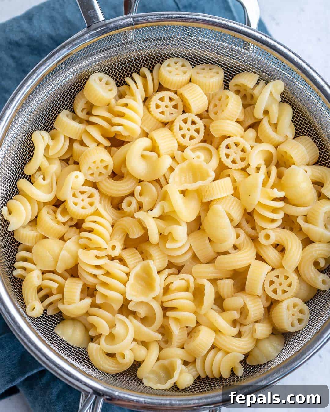 Cooked short pasta being drained in a colander under cold water
