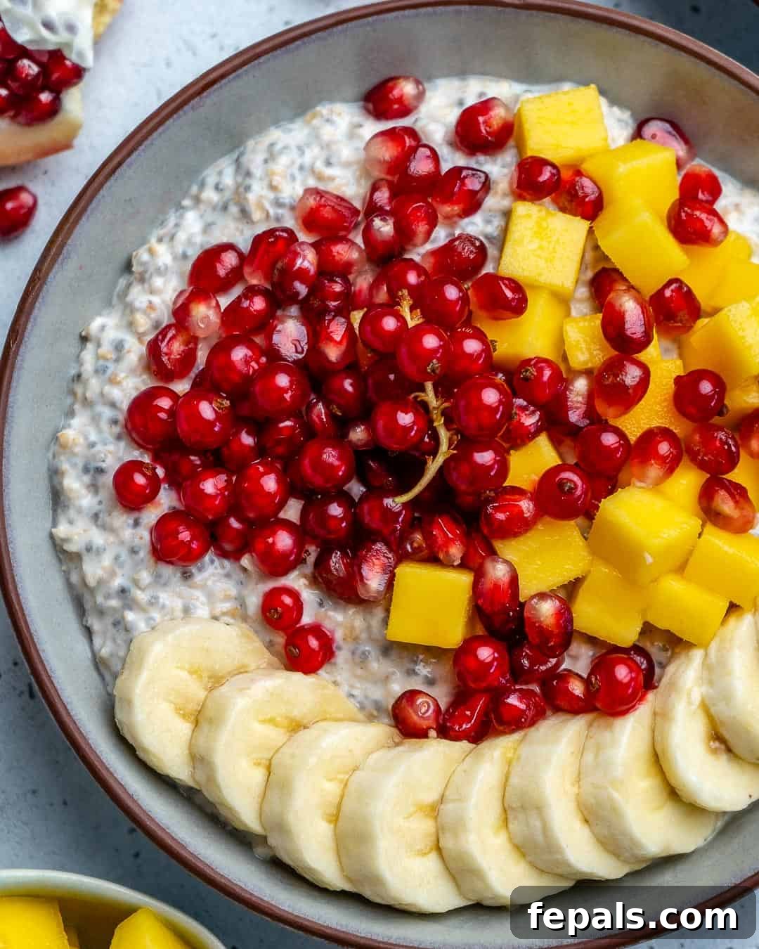 Effortless Greek Yogurt Overnight Oats 2 A round bowl of vibrant overnight oatmeal, generously topped with freshly sliced bananas, diced mango, bright pomegranate seeds, and ruby red currants, inviting you to a nutritious start.
