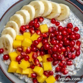 Overnight soaked oatmeal in a round bowl, garnished with sliced bananas, mango, and pomegranate arils.
