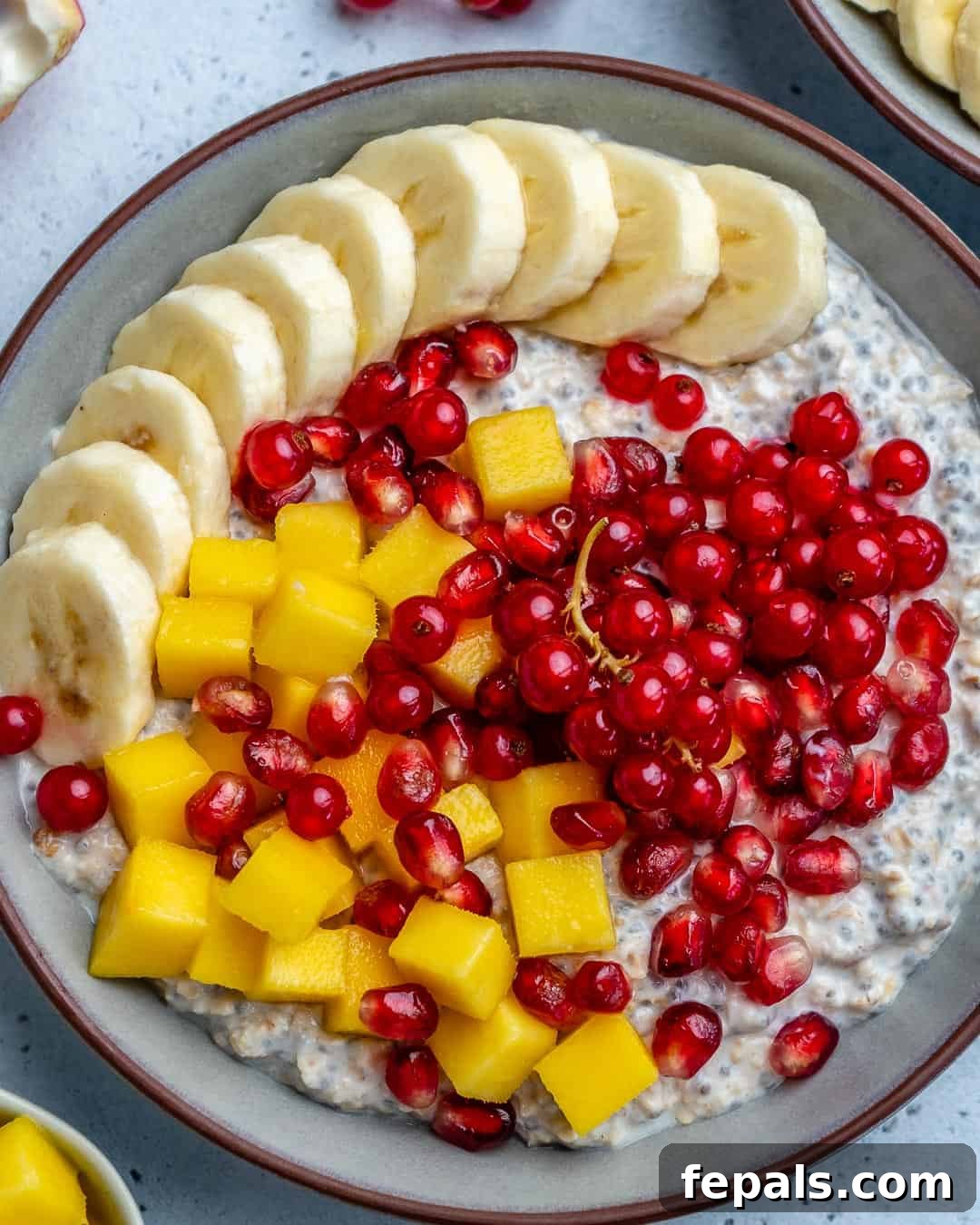 Effortless Greek Yogurt Overnight Oats 8 A close-up of overnight soaked oatmeal in a beautiful round bowl, elegantly garnished with sliced bananas, diced mango, and vibrant pomegranate arils, creating an irresistible breakfast.
