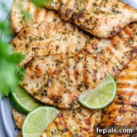 Grilled chicken breasts on a plate with lime wedges and cilantro garnish.