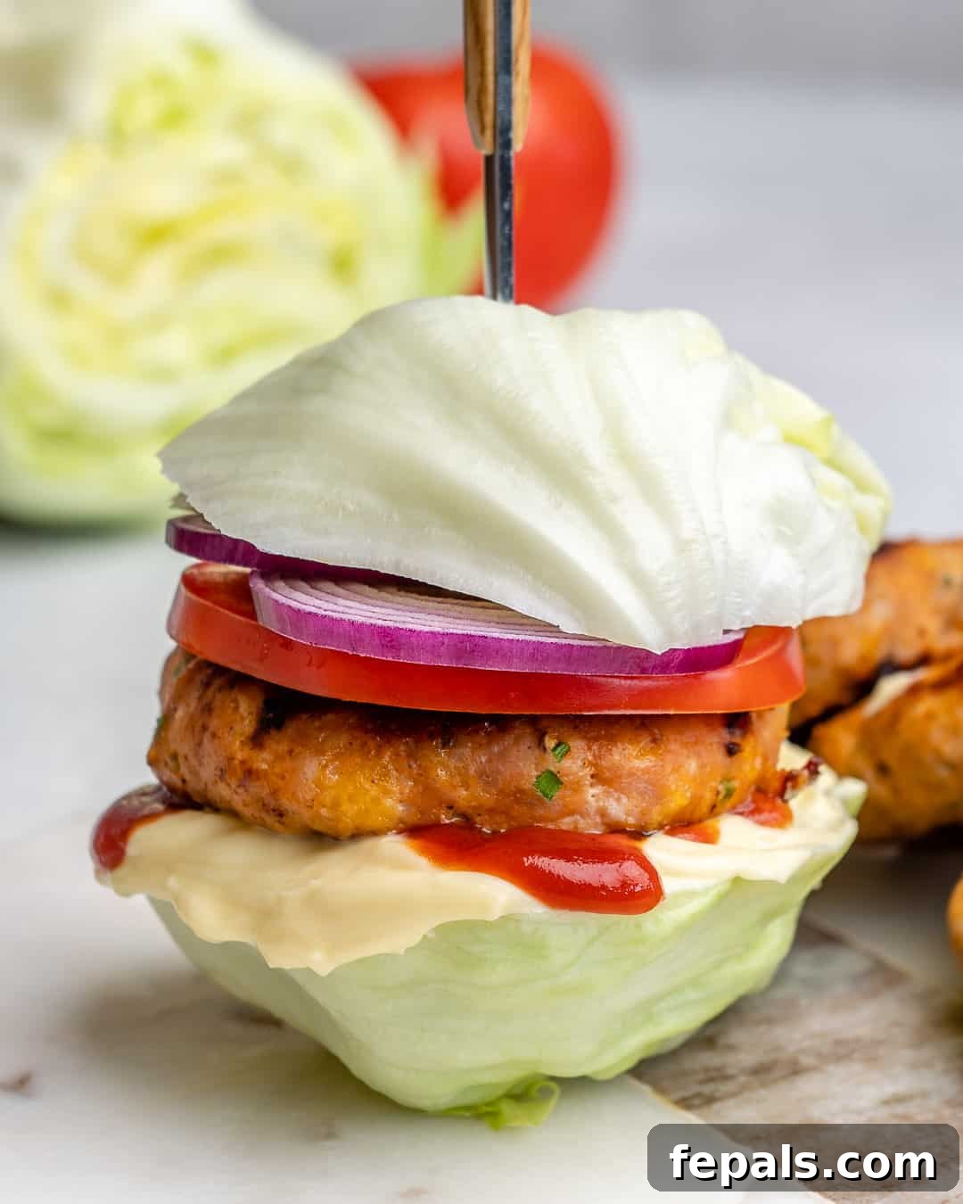 Close-up side view of a healthy chicken burger served in a lettuce bun, garnished with fresh toppings.