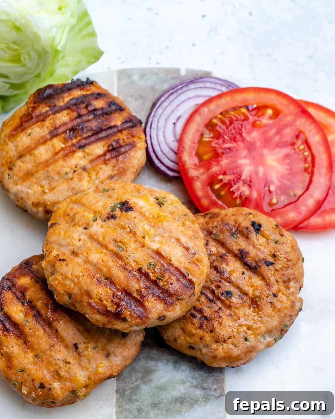 A platter of perfectly grilled chicken burger patties, accompanied by fresh sliced tomatoes and red onions, ready for serving.