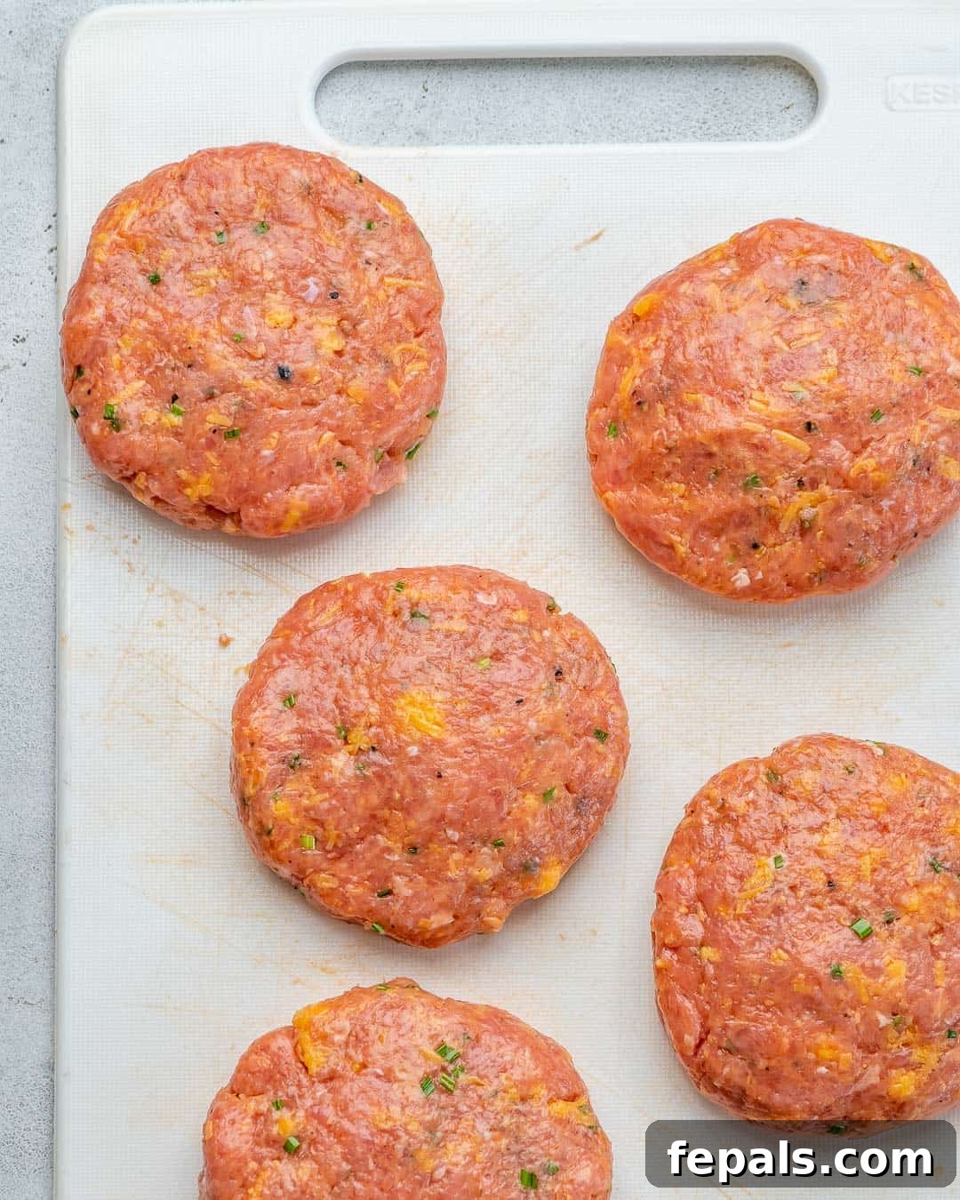 Raw, uncooked chicken patties perfectly shaped and arranged on a cutting board, ready for grilling.