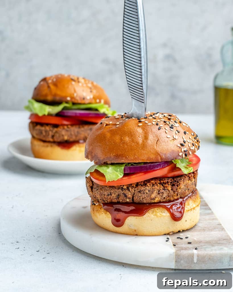 side shot of 2 bean burgers on a flat surface with knife sticking in the middle of one of them
