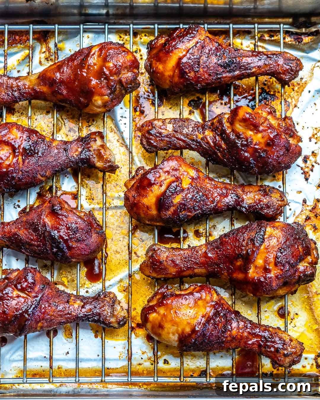 A close-up side view of several golden-brown baked chicken drumsticks arranged on a wire rack, showcasing their crispy skin and delicious texture.