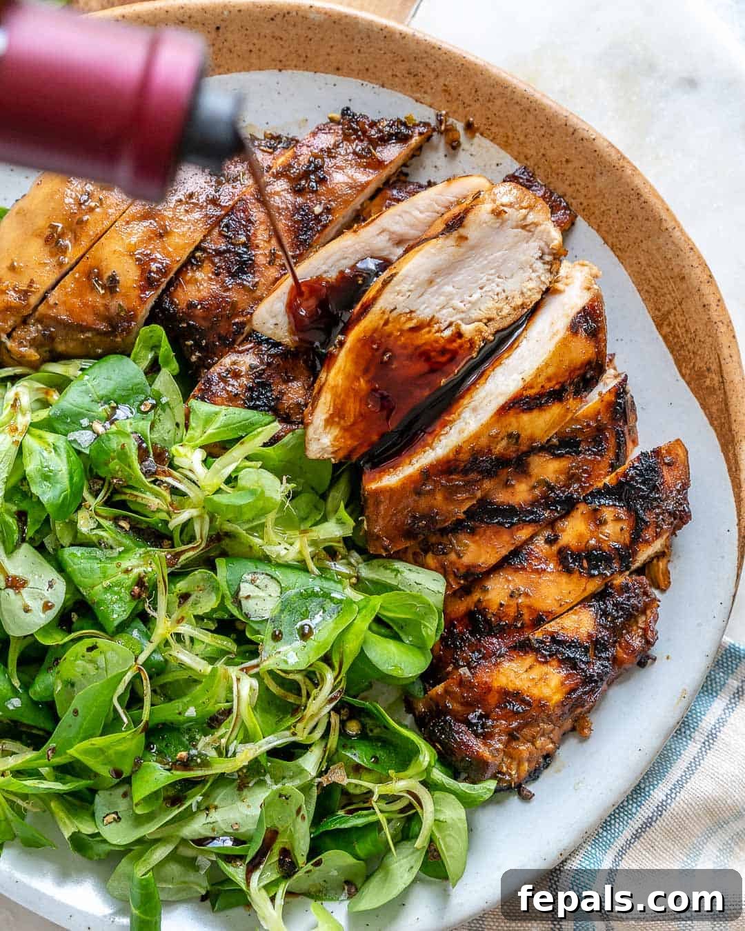 A captivating side shot of a bottle of rich balsamic vinegar being artfully poured over freshly cooked balsamic chicken breasts, creating a beautiful glaze.
