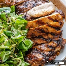 Side view of a perfectly cooked balsamic chicken breast, sliced and served on a plate with a fresh balsamic salad, showcasing its juicy interior.
