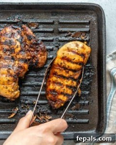 Grilled chicken breast cooking on a grill pan, with a hand holding tongs, ready to flip.