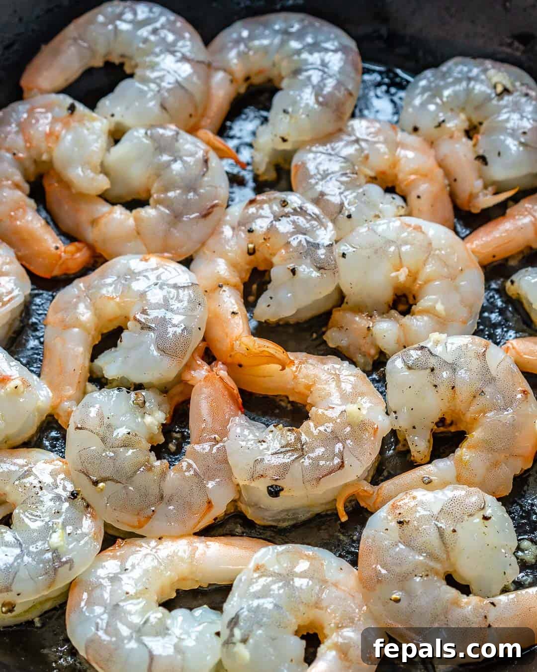 raw marinated shrimp placed on a black cooking skillet before cooking