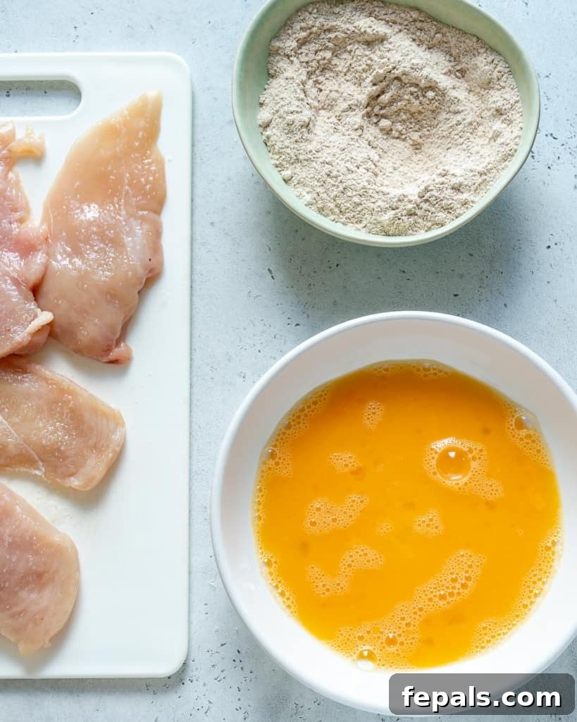 chicken on platter with bowl of egg wash and bowl of flour for breading