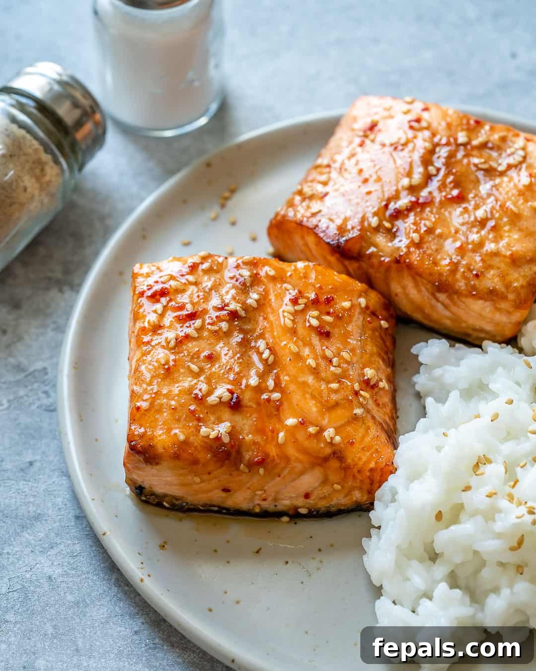 Airfryer'da Nar Gibi Kızarmış Ballı Somon 10 A close-up view of a perfectly cooked honey glazed salmon fillet, garnished with sesame seeds, served alongside white rice on a plate.