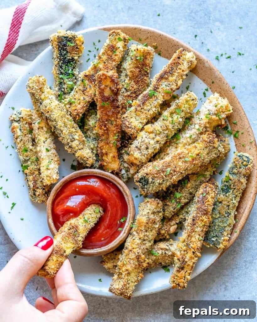 Parmesan-Crusted Zucchini Fries 8 hand holding a zucchini fry in a ketchup dip
