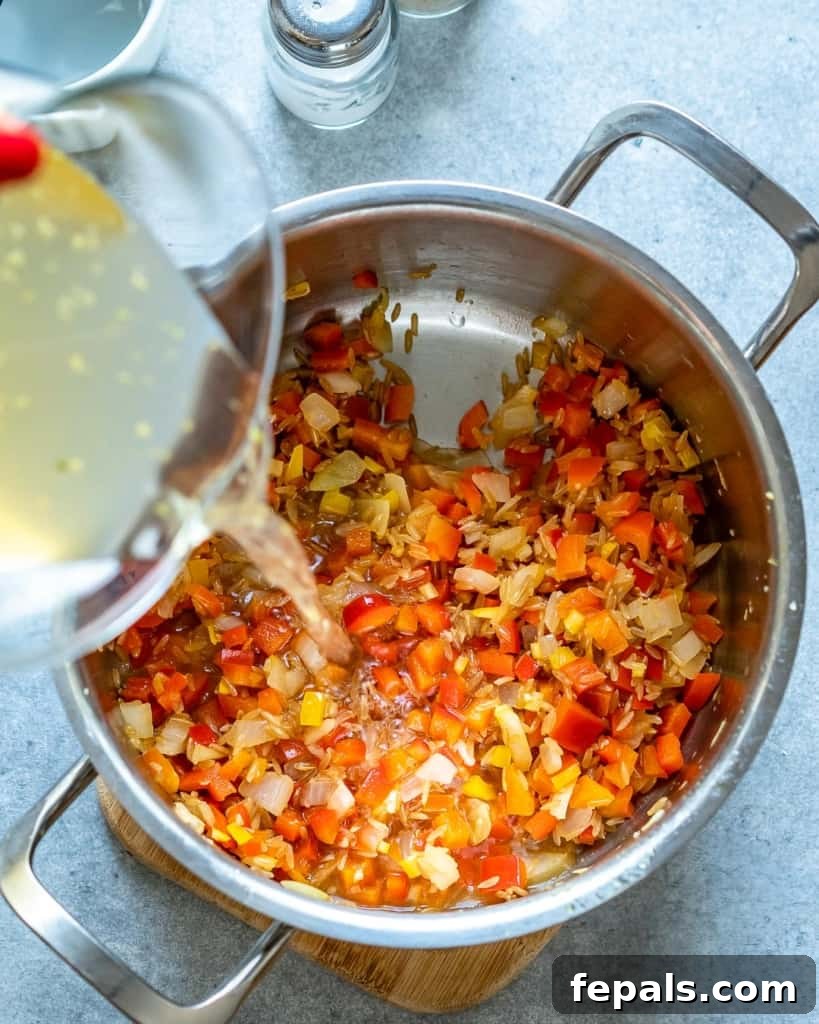 Homestyle Tomato Rice Soup 6 vegetable broth being poured into a pot with sautéed vegetables and rice