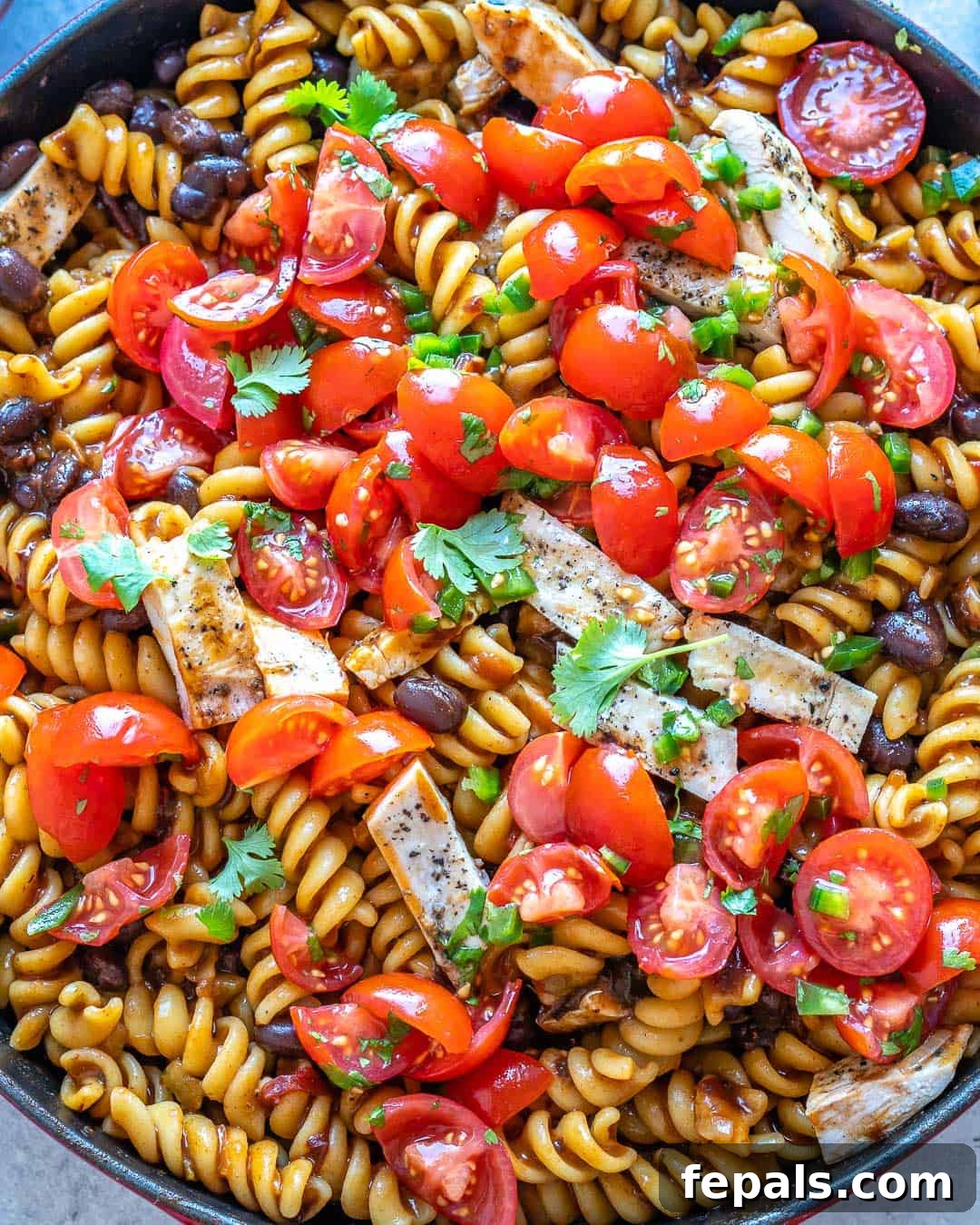 Smoky Chipotle Chicken Pasta 9 Close up of tomatoes and cilantro toppings on pasta in pot.