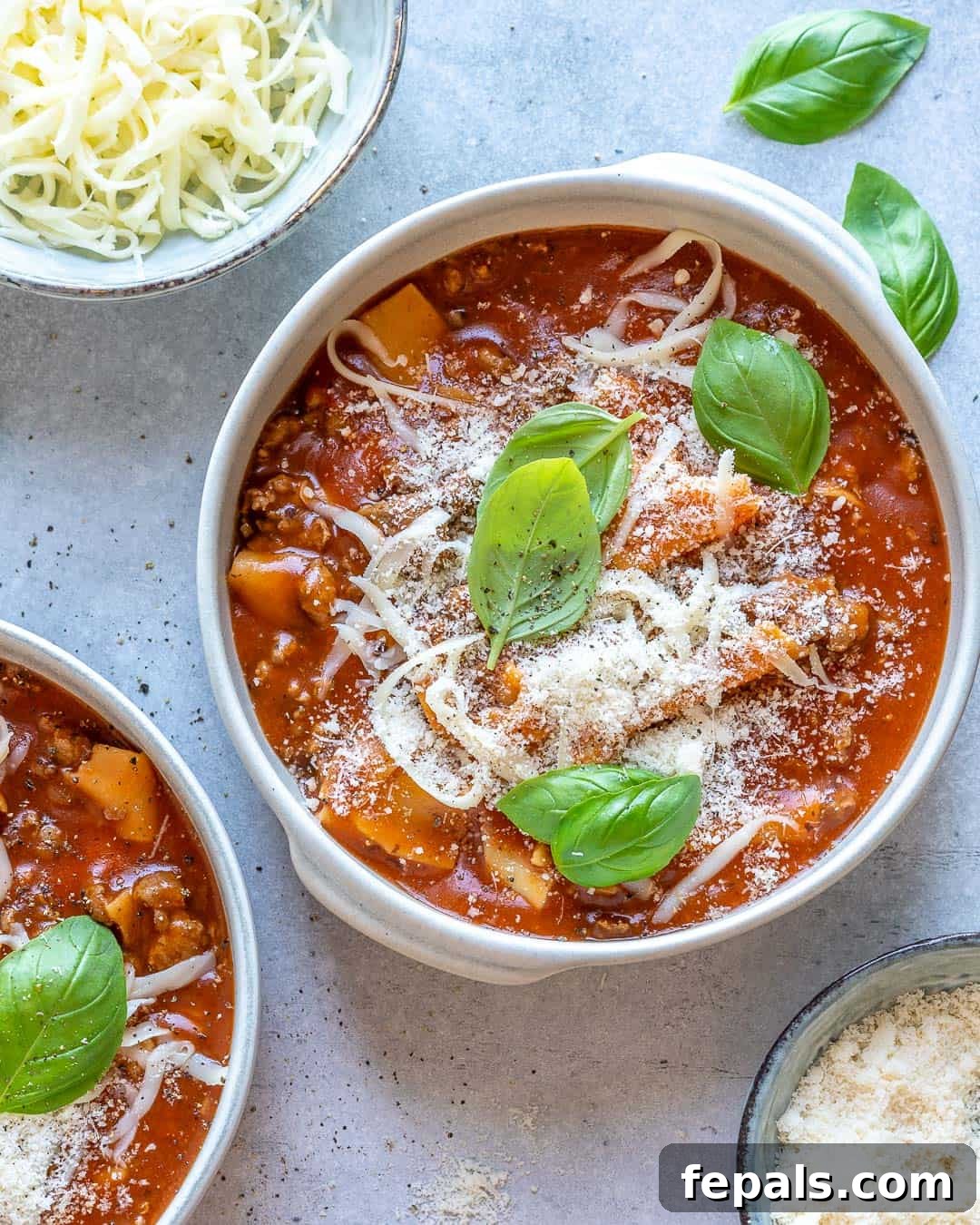 Comforting One Pot Lasagna Soup 7 Two bowls of one pot lasagna soup on counter with cheese and basil.