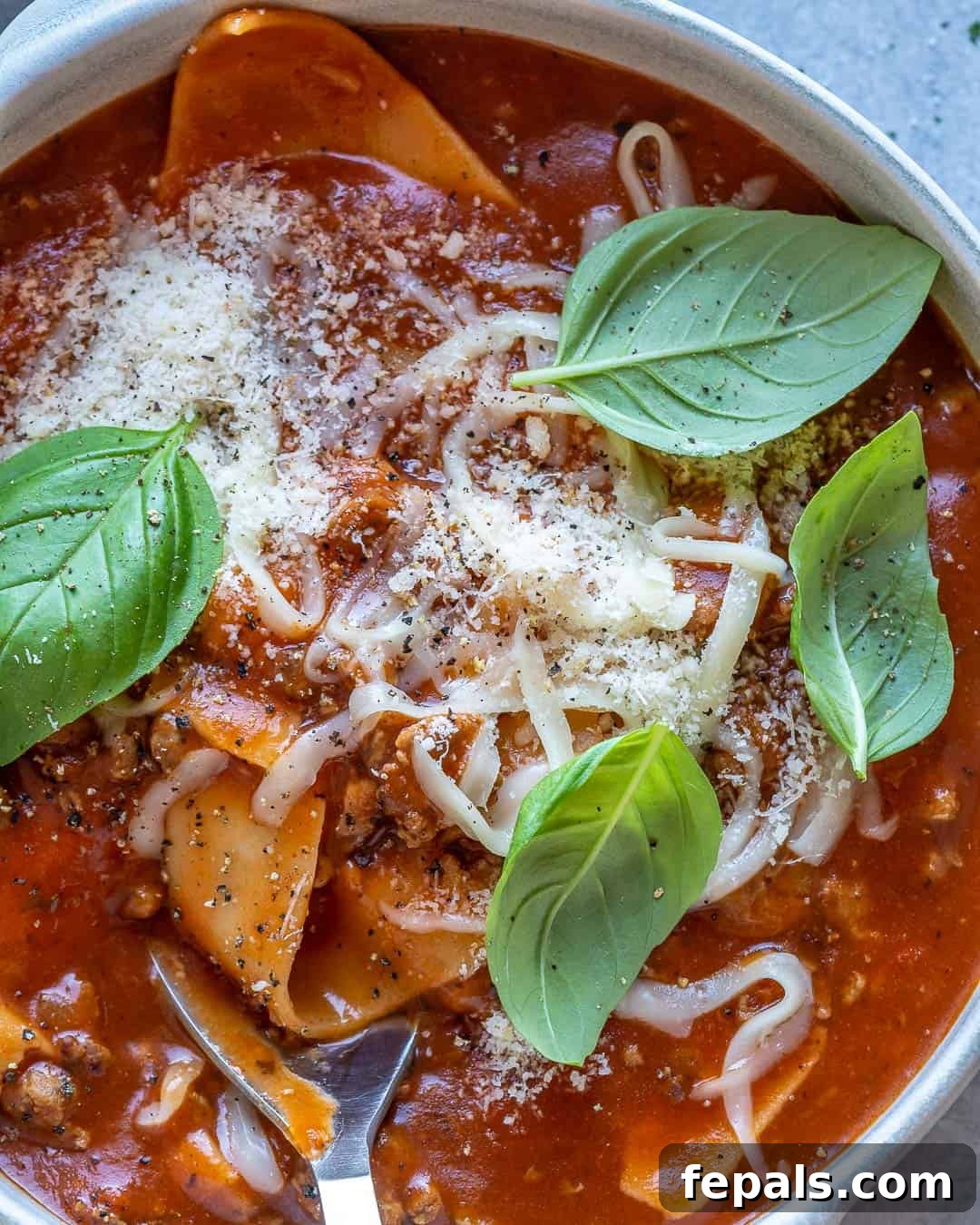 Comforting One Pot Lasagna Soup 9 Close up of lasagna soup in bowl with basil and cheese on top.
