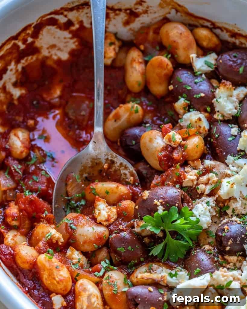 Gigantes Plaki 11 Close-up of baked beans in a dish with Greek garnishes like feta cheese and olives, ready to be served.