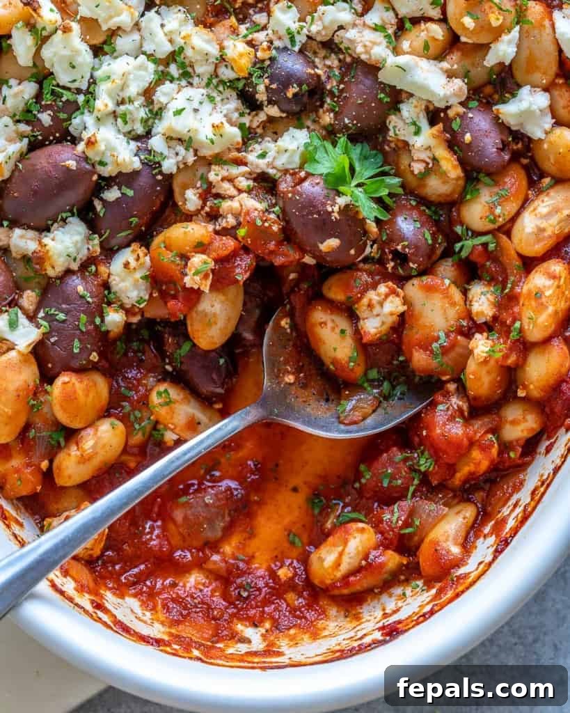 Gigantes Plaki 3 A spoon in a white dish filled with vegetarian Greek Baked Beans, showing the creamy sauce and tender beans.