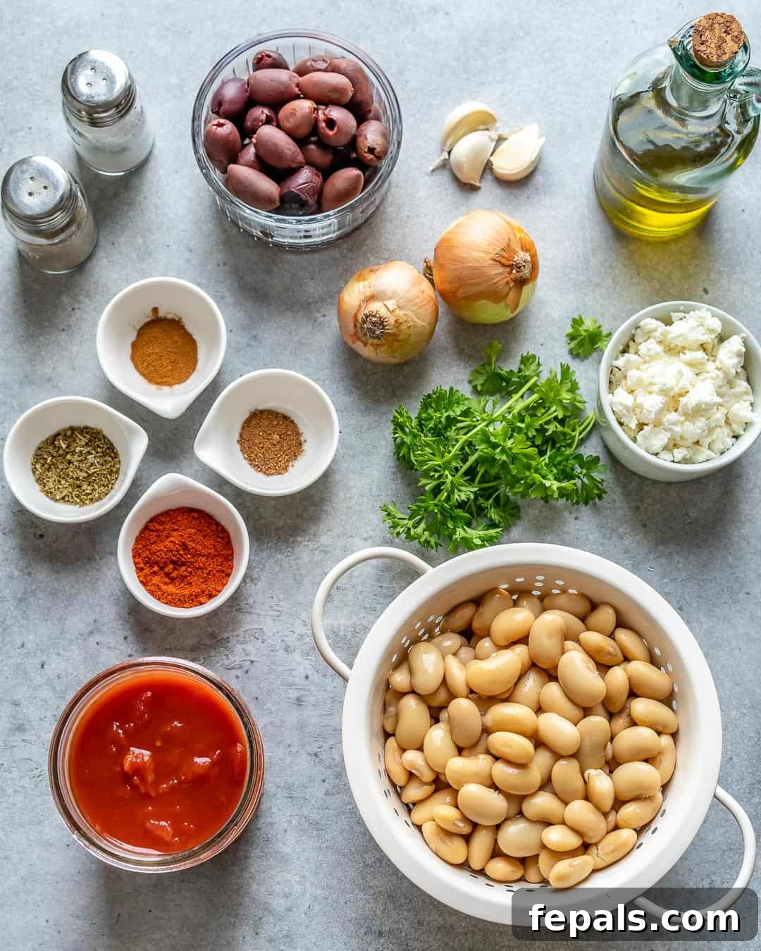 Gigantes Plaki 4 Ingredients for Greek Baked Beans laid out on a kitchen counter, including canned beans, olives, feta, tomatoes, and spices.
