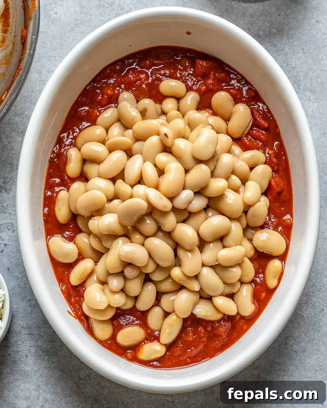 Gigantes Plaki 6 Butter beans and Kalamata olives being stirred into the red tomato sauce in a baking dish.