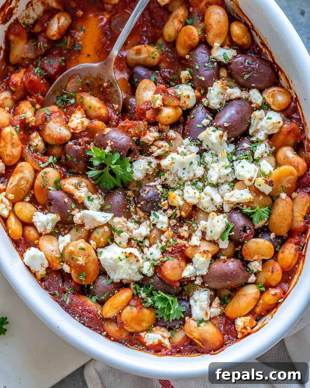 Gigantes Plaki 7 A white baking dish filled with finished Greek Baked Beans, topped with crumbled feta and fresh parsley.