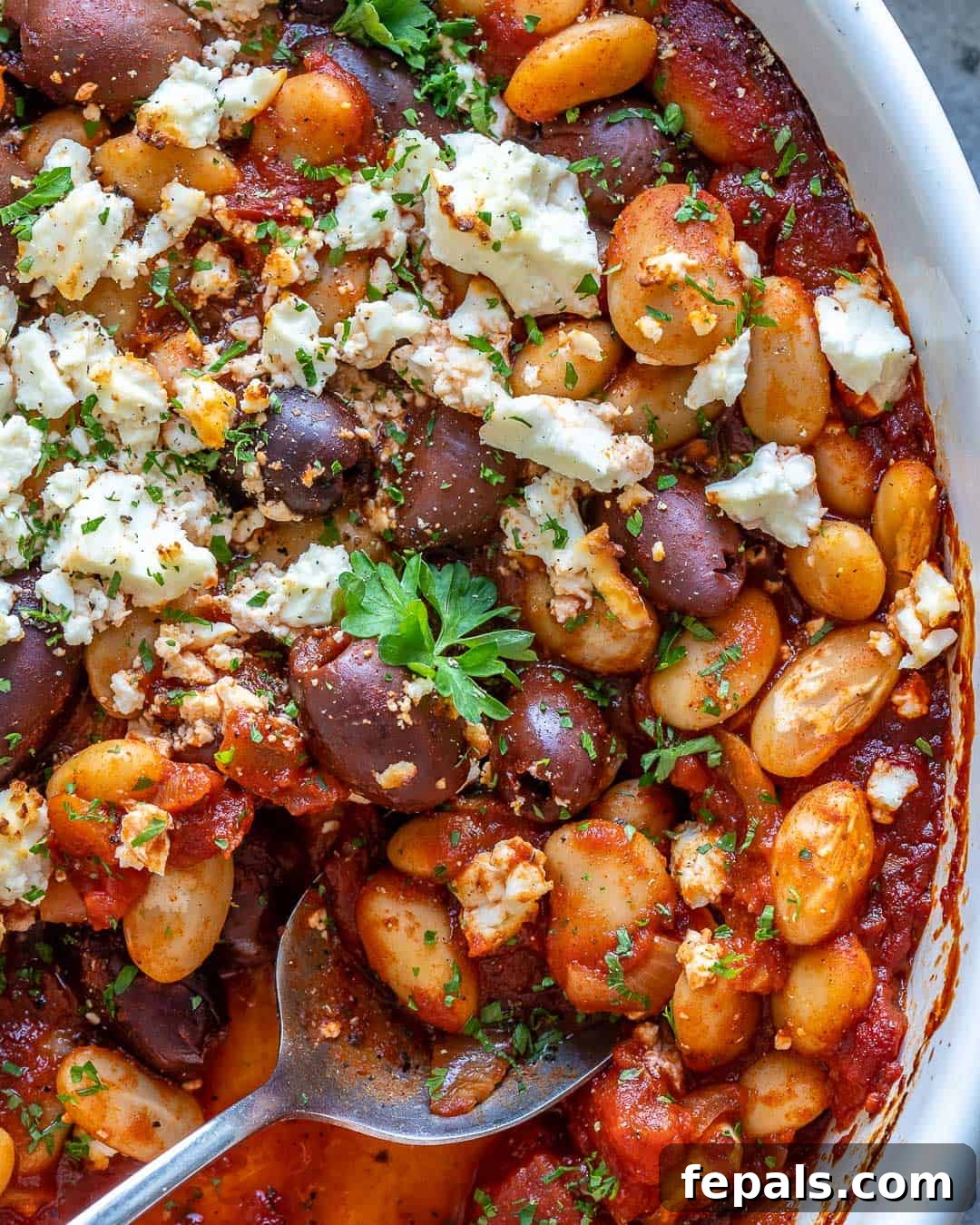 Gigantes Plaki 9 Close-up of Greek Baked Beans in a baking dish with a spoon, highlighting the tender beans and thick sauce.