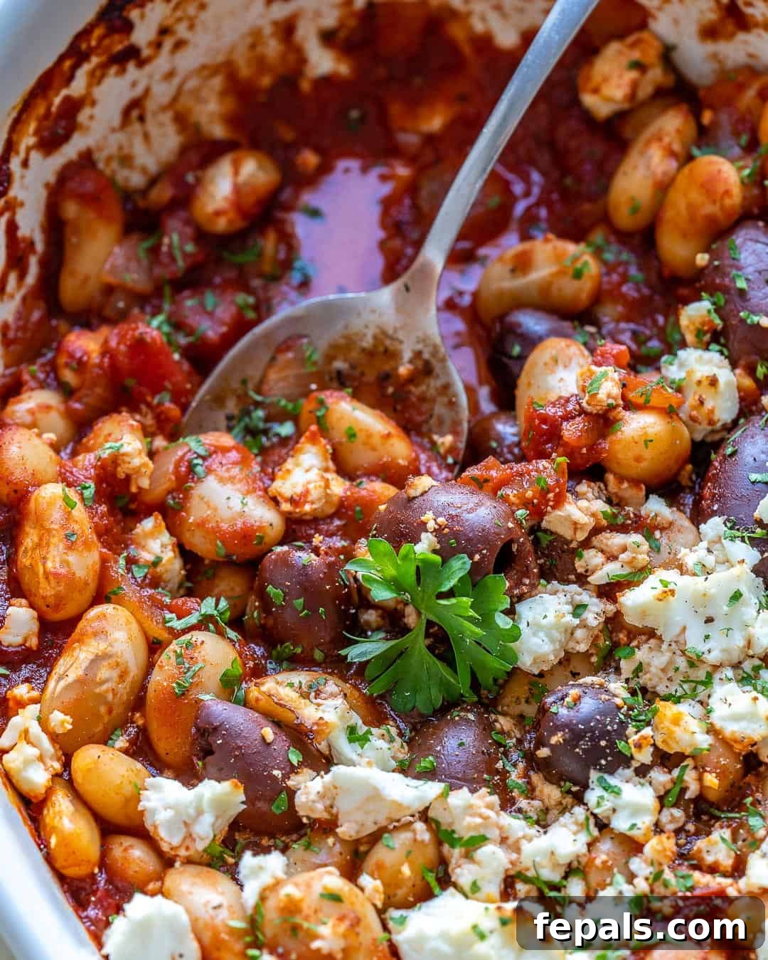 Gigantes Plaki 10 Spoon lifting Greek Baked Beans from a dish, showcasing the rich sauce and whole beans.