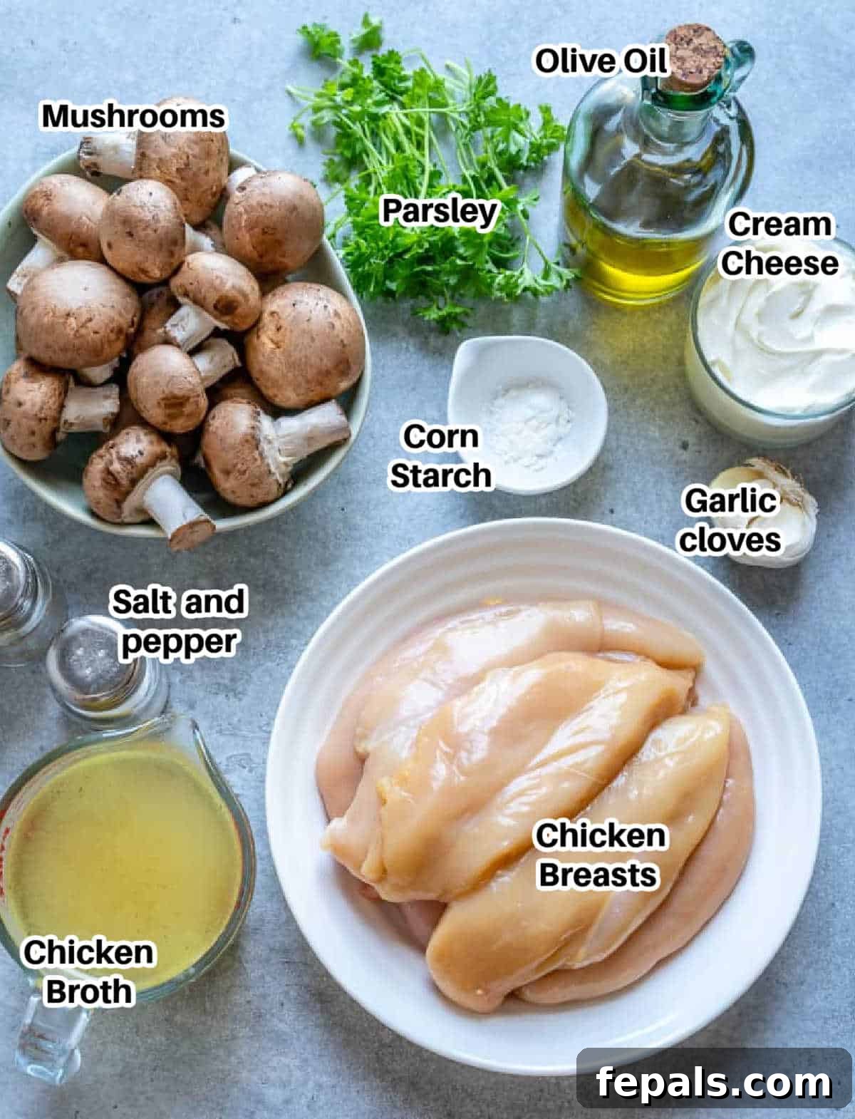 Ingredients laid out on a wooden board to make creamy mushroom chicken, including chicken breasts, mushrooms, garlic, parsley, and various seasonings.