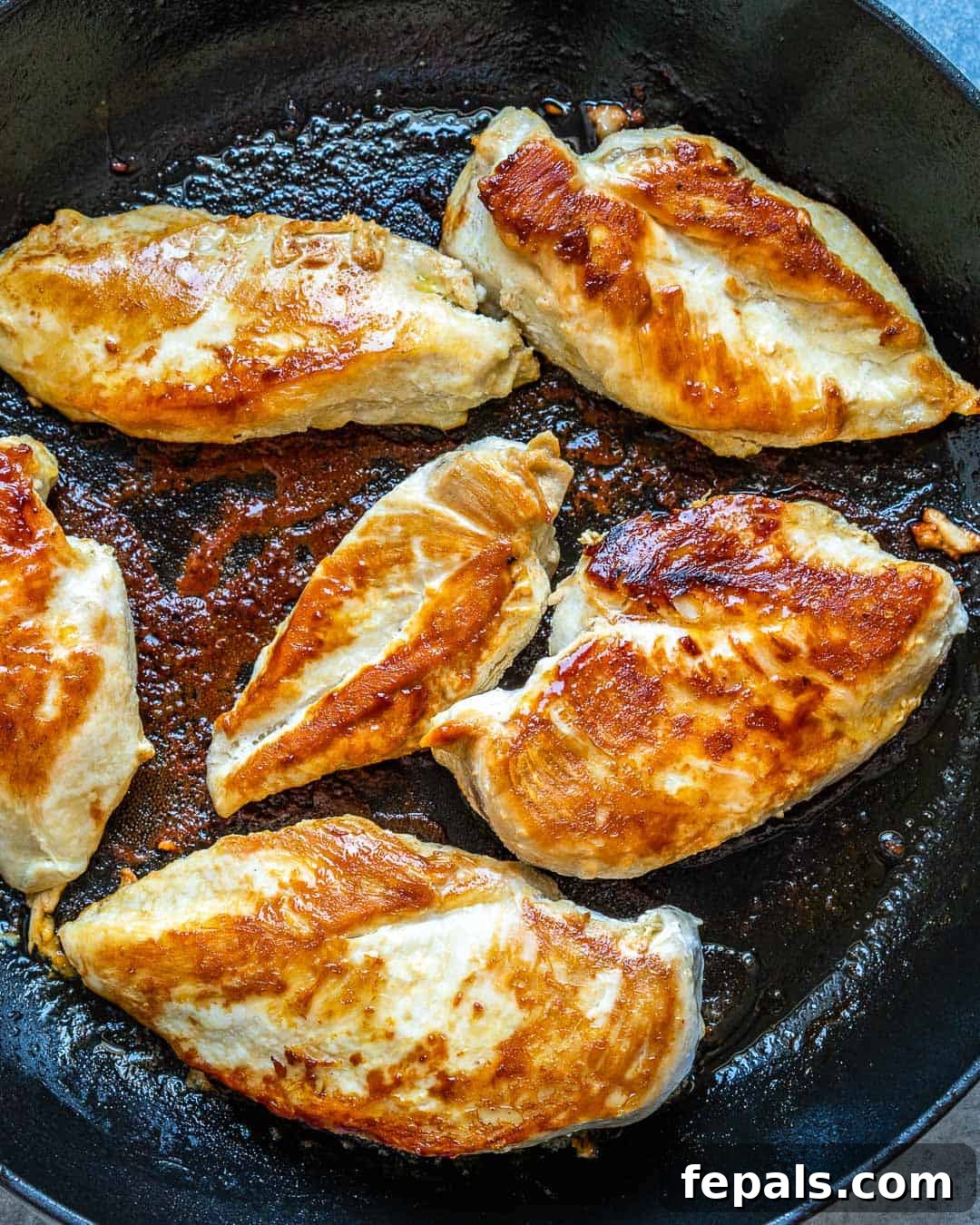 Several golden-brown cooked chicken breasts in a skillet.