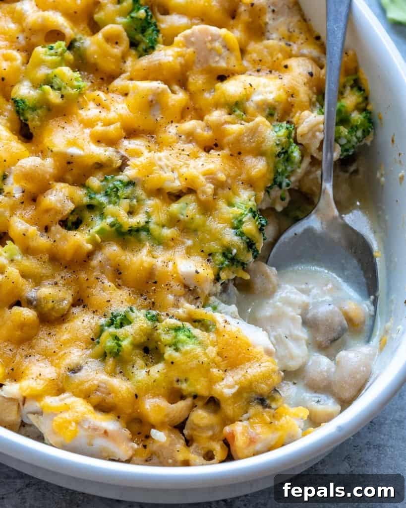 A spoon digging into a freshly baked and bubbly chicken pasta casserole, highlighting its appetizing texture and golden-brown top.