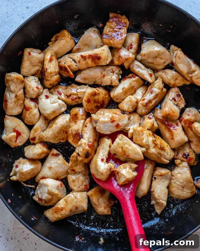 Cubed chicken being stir-fried to golden perfection in a black skillet.