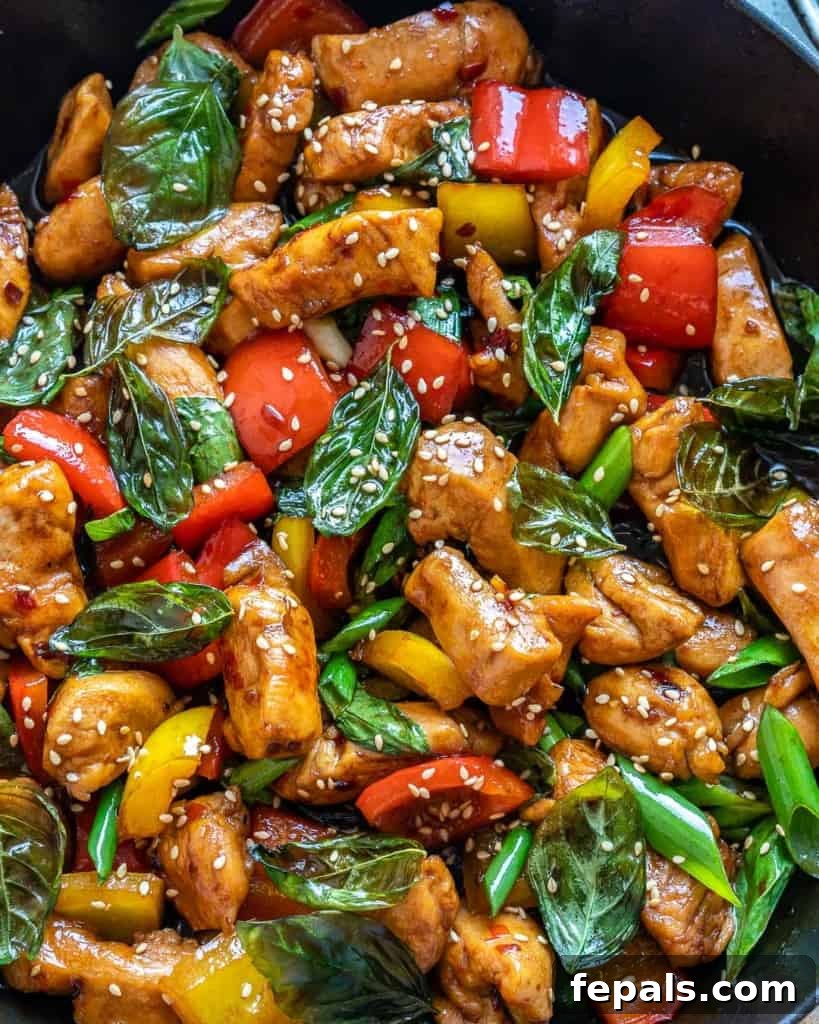 Overhead view of a prepared Thai Basil Chicken dish in a bowl, garnished with green onions and sesame seeds.