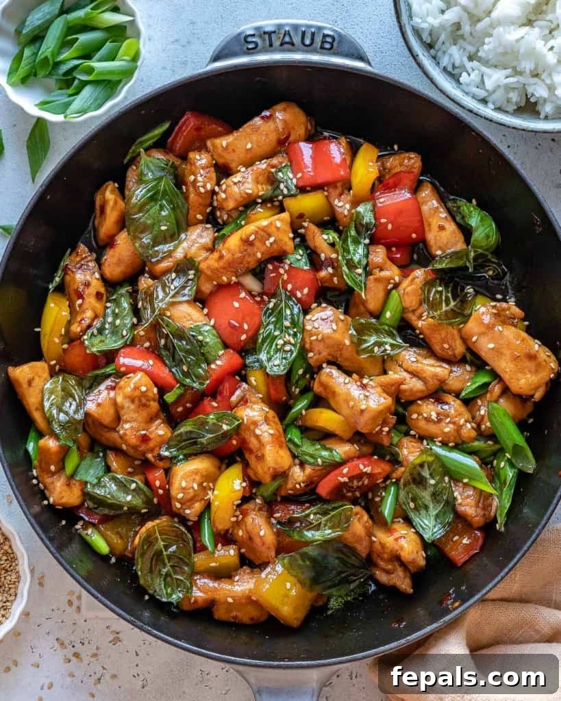 Close-up top view of Thai basil chicken stir-fry in a black skillet with vibrant green basil.