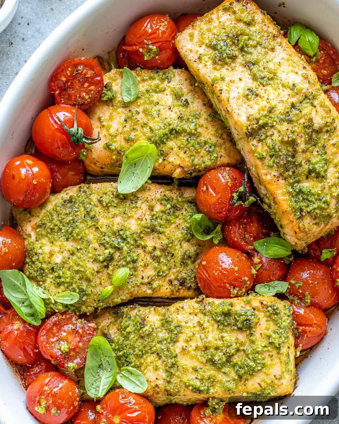 Baked Pesto Salmon in white serving dish with cherry tomatoes and fresh basil garnish
