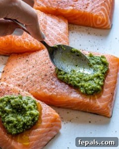 Spoon spreading pesto sauce evenly on salmon fillets