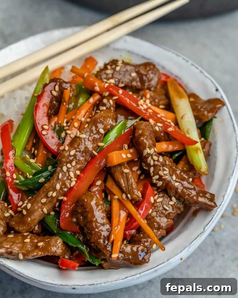 Side view of Mongolian beef in a white bowl with chopsticks, showcasing the rich sauce and vibrant vegetables.