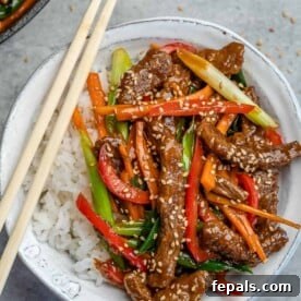 Top view of a white bowl of white rice topped with Mongolian beef with chopsticks on the left, ready to serve.