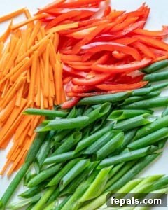 Sliced bell peppers, julienned carrots, and chopped green onions on a cutting board, neatly prepped for stir-frying.