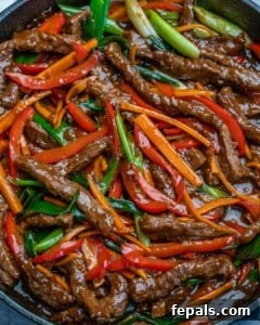Close-up view of beef stir fry combined with carrots, red bell peppers, and green onions, simmering in the sauce.