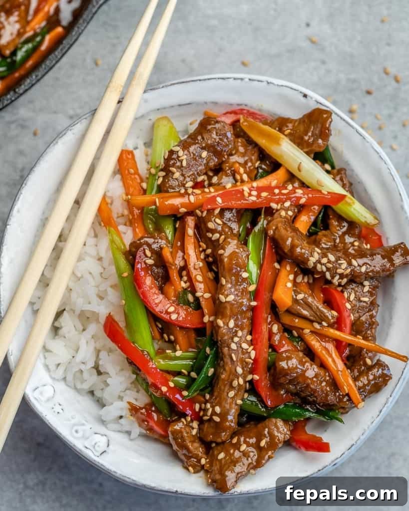 Top view of a white bowl of white rice topped with Mongolian beef, featuring vibrant colors and chopsticks resting on the side.