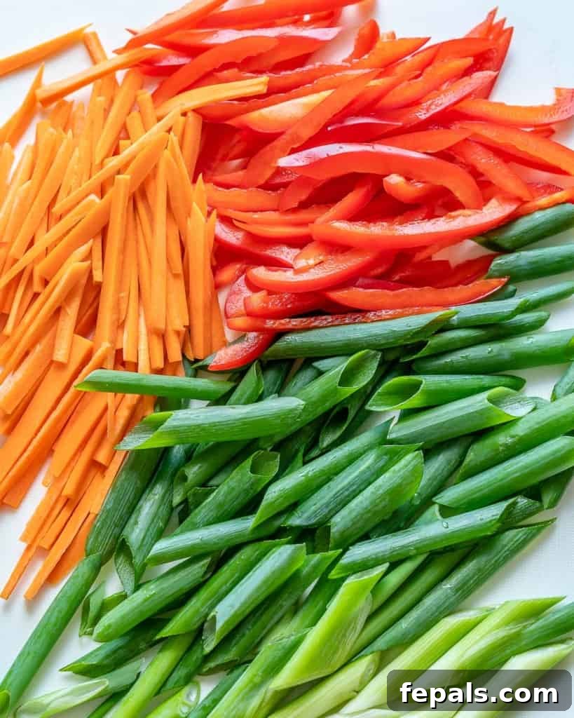 Assortment of thinly sliced bell peppers, julienned carrots, and chopped green onions neatly arranged on a cutting board, ready for stir-frying.
