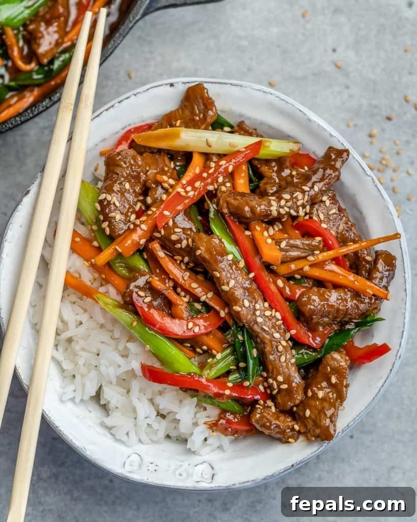 Top view of a round white bowl filled with rice and stir-fried beef with vibrant vegetables, perfectly arranged for a delicious meal.
